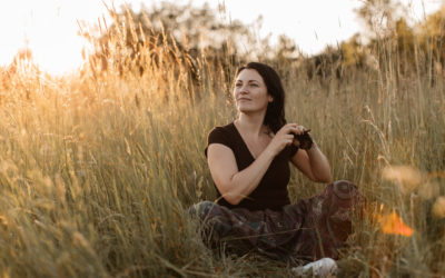 A portrait of a happy woman sitting in grass and doing her hair. A young woman enjoying plaiting hair in the nature at sunset. A portrait of a happy woman sitting in grass and doing her hair. A young woman enjoying plaiting hair in the nature at sunset.